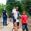 Homens, mulheres e crianças caminhando em Estrada com lama, com Polícia da ONU ao fundo
