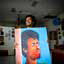 Homem segurando pintura grande de rosto de homem contra um fundo azul