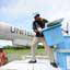 Homem de pé em plataforma com várias caixas azuis, em frente a uma asa de avião com a palavra United pintada