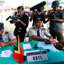Operadores de camera e mulheres filmam dois oficiais que examinam passaportes em mesa verde com placa que diz &ldquoIMMIGRATION RDTL&rdquo